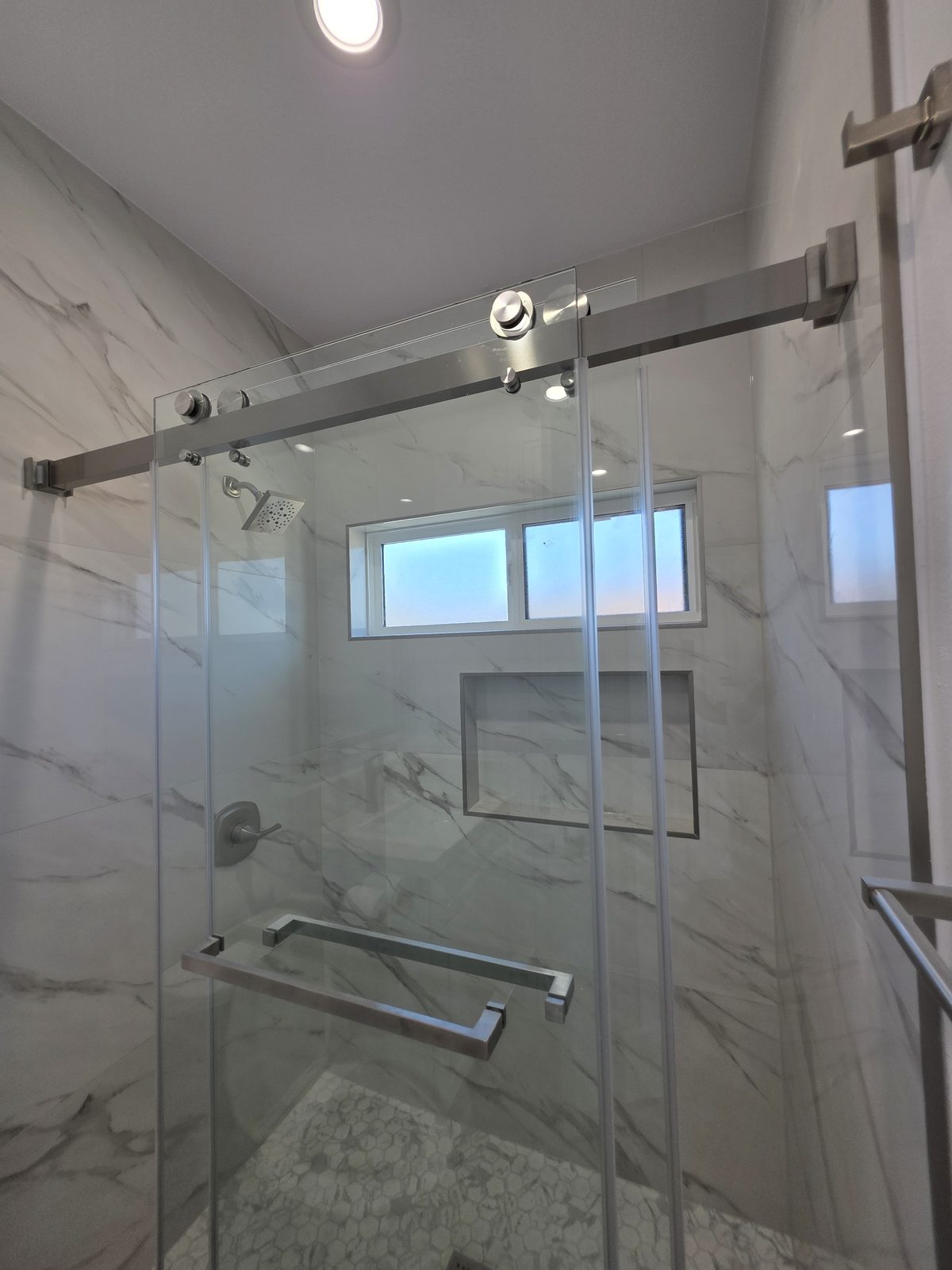Finished walk-in shower with marble-look tile and glass door